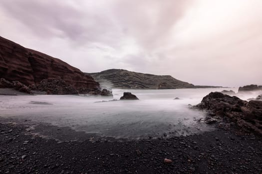 shore of the volcanic beach of Ciclos against cloudy sky and foggy ocean in Yaiza, Lanzarote at Canary Islands, Spain, concept of wild nature and marine lifestyle