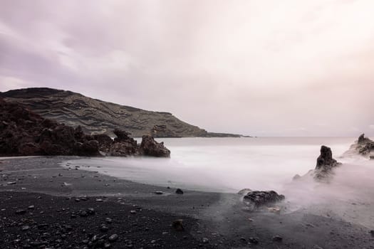 shore of the volcanic beach of Ciclos against cloudy sky and foggy ocean in Yaiza, Lanzarote at Canary Islands, Spain, concept of wild nature and marine lifestyle