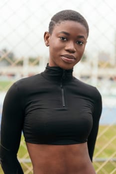 young tender ethnic female in black wear with short hair looking at camera on urban lawn in summer