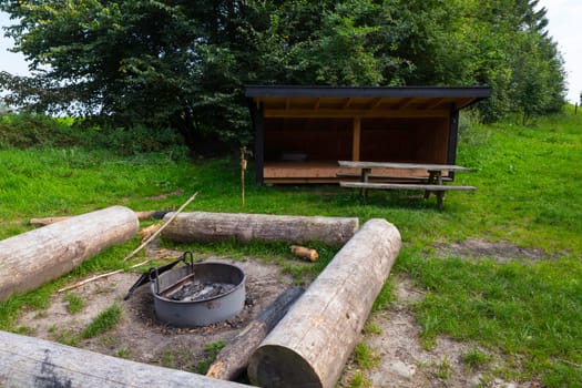 A quiet outdoor campsite featuring a wooden shelter, picnic table, and campfire pit. Ideal for camping, featuring a natural setting surrounded by lush greenery in demark