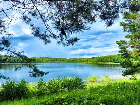 A tranquil lake reflects the greenery and distant hills under a partly cloudy sky during a beautiful summer day.
