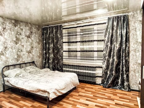 This cozy bedroom showcases a spacious bed with patterned bedding, elegant curtains, and beautiful wooden flooring for a stylish ambiance.