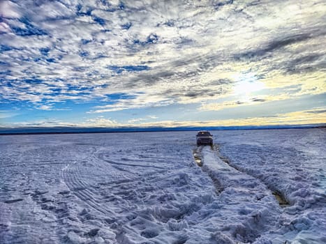 The snowy road stretches alongside a river with melting ice, highlighting winter activities in Arkhangelsk and the expansive sky above.