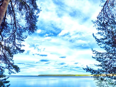 A tranquil lake is bordered by tall trees, with fluffy clouds reflecting in the calm water.