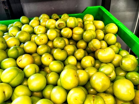 A crate overflowing with fresh green plums is displayed at a bustling market, highlighting their vibrant color and freshness.