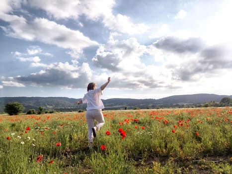 A happy girl in a poppy field. The journey of a middle-aged woman in summer. A tourist on trip