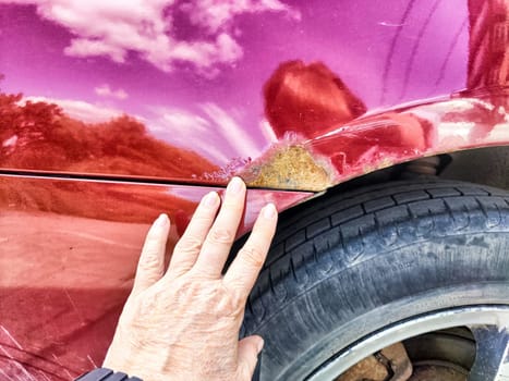 A person is pointing directly at a rusty, weathered place on a car that shows signs of age and decay, highlighting its condition