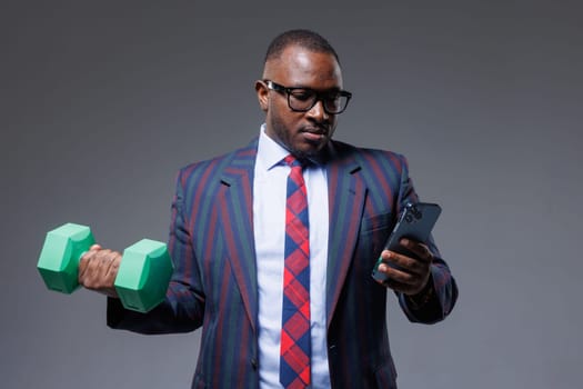 African businessman in suit works online with phone in hand and does sports at the same time, business and sports
