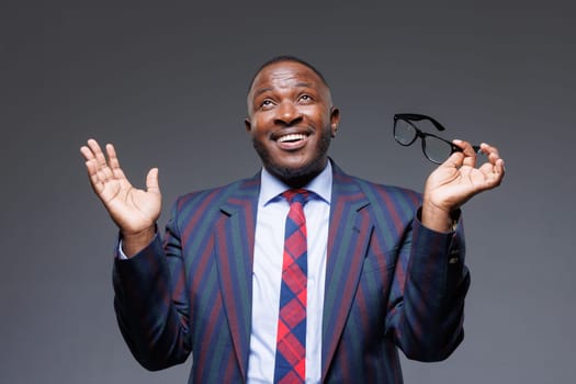 Smiling african american guy in suit taking off glasses on gray background, vision improvement after eye surgery, astigmatism