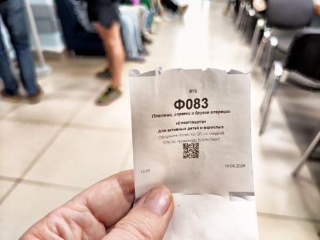 Kirov, Russia - September 18, 2024: A customer holds a ticket indicating their place in the bank's private service queue, navigating through midday busyness.