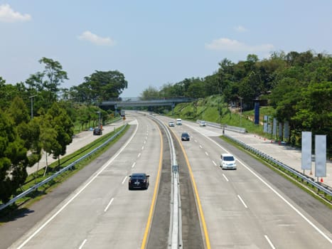 A highway with a bridge over it and cars driving on it. The cars are mostly white and black