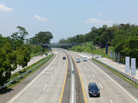 A highway with a bridge over it and cars driving on it. The cars are mostly white and black