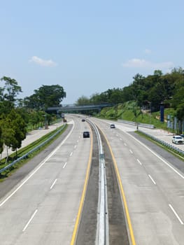A highway with a bridge over it and cars driving on it. The cars are mostly white and black