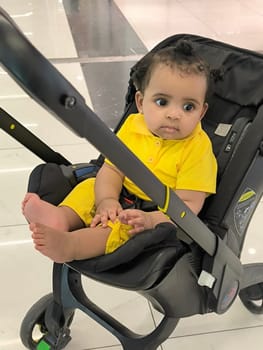 18 August 2024 Tbilisi Georgia, central station, dark skinned baby toddler in stroller yellow clothes. High quality photo