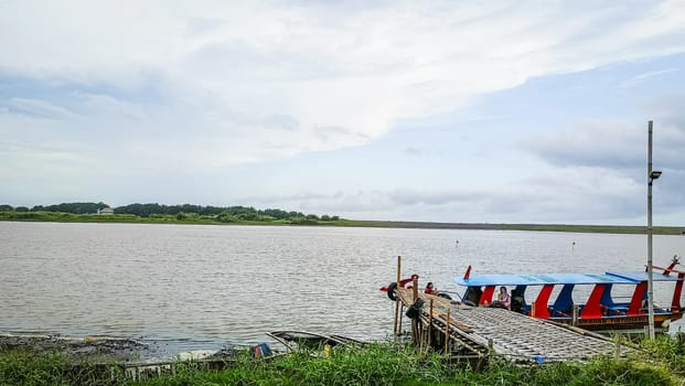 A beach with a boat in the water. The sky is cloudy and the water is calm