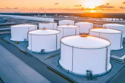 Large white industrial tanks storing oil and fuel in a refinery at sunset