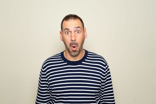 Hispanic man with beard about 40s scared and shocked with surprise expression, fear and excited face. Isolated on beige background