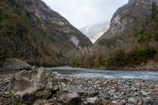 A serene mountain river with crystal blue water flowing through an autumn landscape. The vibrant fall colors of the surrounding trees create a stunning contrast with the cool, clear water, capturing the beauty of nature during the autumn season