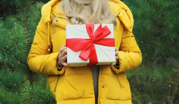 Close up woman holding festive red gift box in her hands in winter forest on Christmas tree background