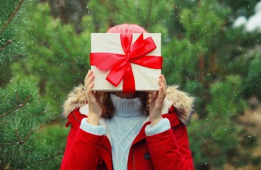Close up woman holding festive red gift box in her hands in winter forest on Christmas tree background