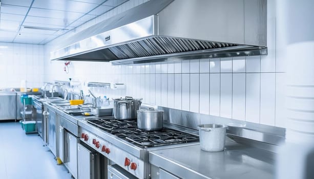 Large industrial kitchen with stainless steel pots on gas stove and exhaust hood in restaurant