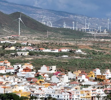 View of a small town and a wind power plant with wind turbines on the hills, on the coast of the Atlantic Ocean, Mediterranean Sea. Development of green ecological alternative energy.