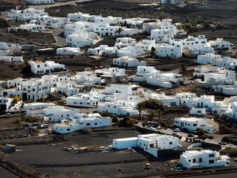 Stylish white buildings and roofs, small towns in Lanzarote among volcanic mountains, black hills and lava formations, aerial photo from above, drone view of villages, travel to the Canary Islands.