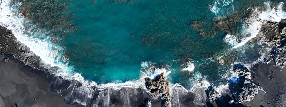 A drone view of the waves during a storm in the Atlantic Ocean, a beach with black basalt sand and rocks on the islands, a scenic marine landscape without people with deep blue turquoise water.