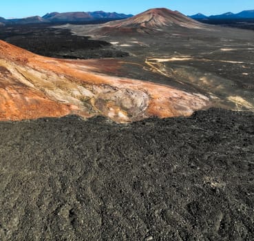 Stunning View from a drone on a red rocky mountain and black volcanic soil, lava formations and mountainous desert landscape and volcanoes of Lanzarote island, Canary Islands.