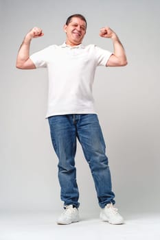 Happy older man showing off his strong biceps while standing against a light gray background close up
