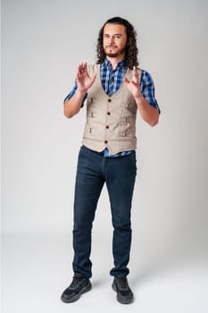 A young man with curly hair dressed in a vest and plaid shirt shows determination while making a fist indoors close up