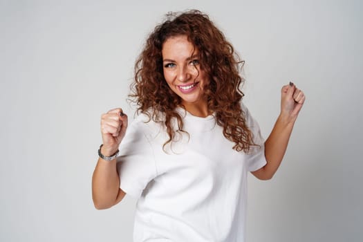 Young woman joyfully celebrates in casual attire against a neutral background close up