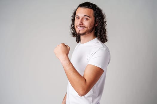 Happy man celebrating success with raised fists in a studio against a plain background close up