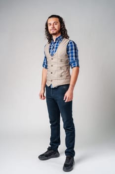 Young man in plaid shirt and vest poses confidently against a neutral background in a studio setting