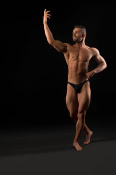 Handsome muscular athlete full-length shot against black wall