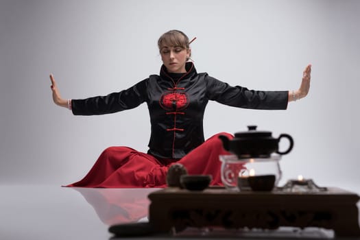 Woman wearing traditional chinese clothes practicing wushu by table laid for chinese tea ceremony shot
