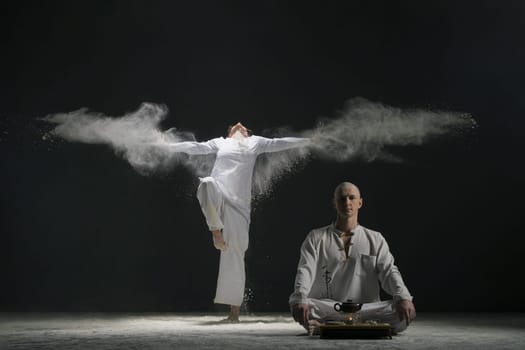 Two male doing yoga in white dust cloud in dark room full-length shot