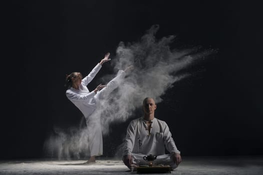 Two male doing yoga in a white dust cloud in dark room full-length view