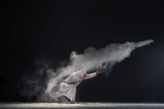 Male doing yoga in white dust cloud in dark room full-length shot - concept of power