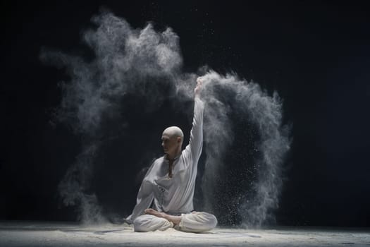 Man doing yoga in white dust cloud in dark room full-length shot - concept of energy