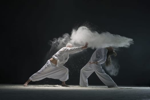 Two male doing yoga in white dust cloud in dark room full-length view