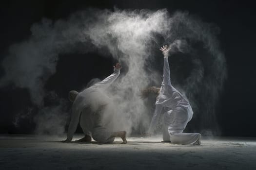 Two men doing yoga in white dust cloud in dark room full-length shot