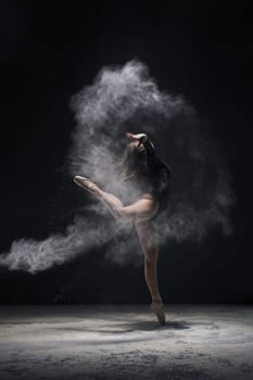 Woman in undrewear and pointe shoes jumping gracefully in a white dust cloud profile shot in dark room