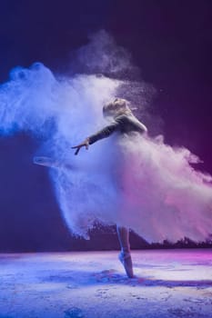 Woman in undrewear and pointe shoes jumping gracefully in a white dust cloud and color light profile view