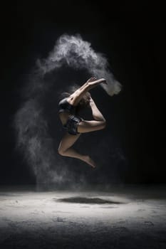 Woman in black shorts and top jumping gracefully in a white dust cloud profile shot in dark room