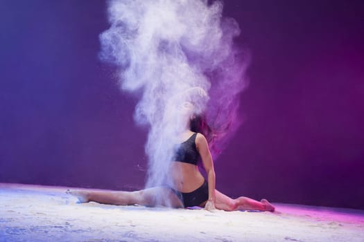 Woman sitting in a split in a white dust cloud profile view