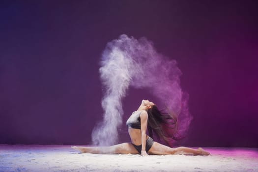 Young girl sitting in a split in a white dust cloud profile view