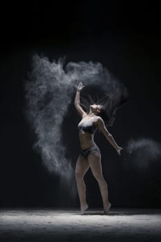 Woman in black shorts and top jumping gracefully in a white dust cloud shot in dark room