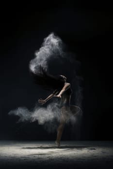 Brunette in black shorts and top jumping gracefully in a white dust cloud shot in dark room