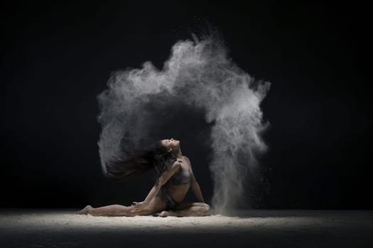 Young brunette sitting in a split in a white dust cloud profile view